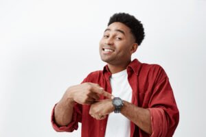 what time is it portrait young attractive dark skinned man with dark afro hairstyle white t shirt red shirt pointing hand watch with happy face expression showing it time eat what time is it portrait young attractive dark skinned man with dark afro hairstyle white t shirt red shirt pointing hand watch with happy face expression showing it time eat